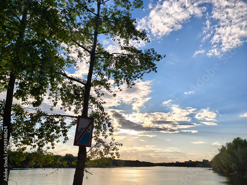 A riverbank with trees in the background. A beautiful pre-sunset cloudy sky. A warm summer evening