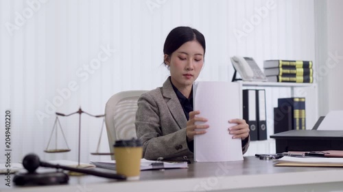 young Asian female lawyer professional review legal document contract paperwork at office desk with gavel scale justice symbol workplace business attorney