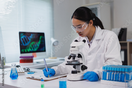 Scientist observing through microscope and writing notes in laboratory