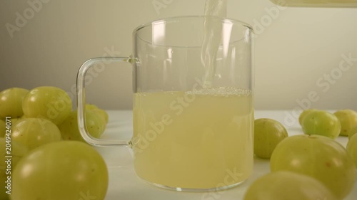 Fresh Indian gooseberry juice pouring into a glass cup from a bottle. Amla juice. Phyllanthus emblica.