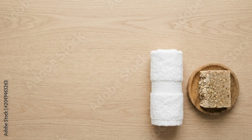 Rolled white terry cloth towel and handmade oatmeal soap on a wooden table, spa and hygiene concept