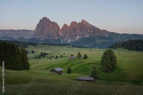 Beautiful sunset view of Seiser Alm (Alpe di Siusi) with wooden huts, green meadows and dramatic Dolomite mountains in South Tyrol, Italy. Scenic landscape of European Alps in summer.