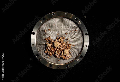Metal sieve with roasted coffee beans on black.