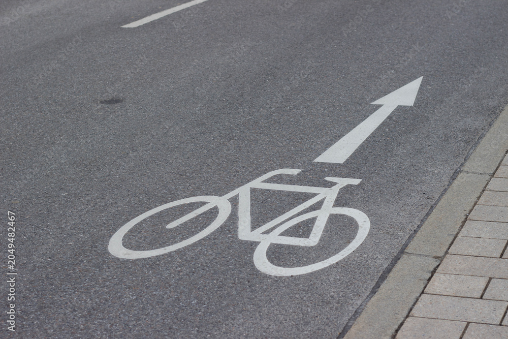 Obraz premium Bicycle lane marking on asphalt road with directional arrow indicating safe path for cyclists alongside cobblestone sidewalk in urban environment