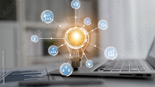 Fotografie A visually engaging image of a light bulb representing innovation, connected to digital icons, placed on a laptop in a modern workspace environment, highlighting creativity and technology