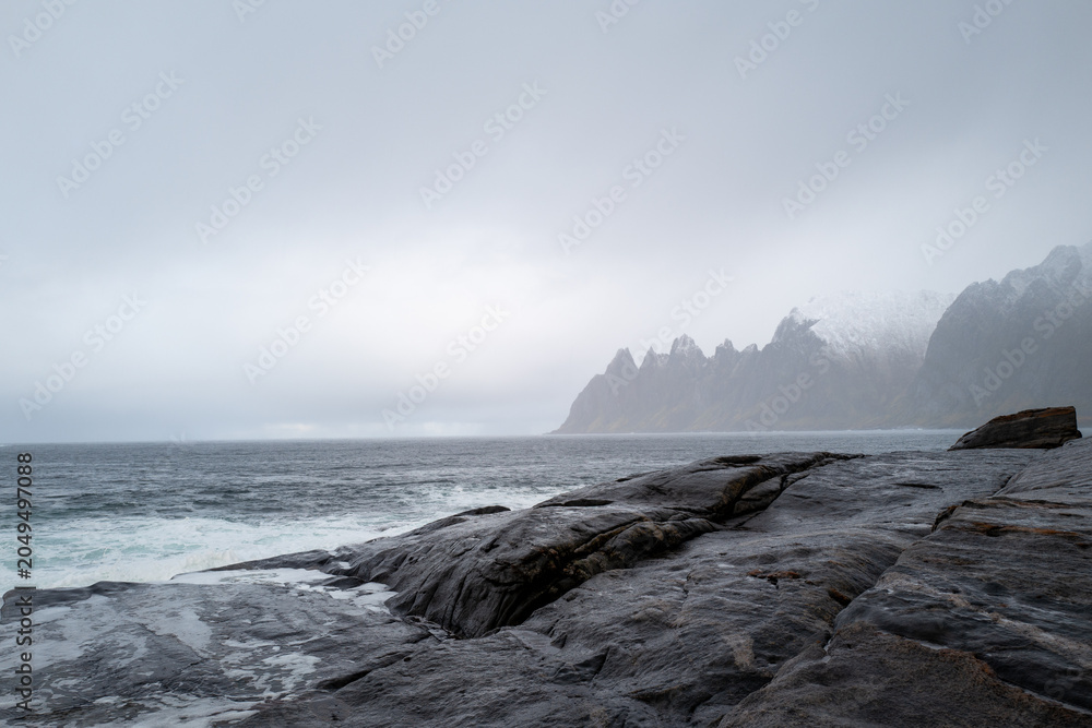 Fototapeta premium The dramatic 'Devil's Teeth' rock formations at Tungeneset viewpoint on the stormy Norwegian coast with misty mountains in the distance.