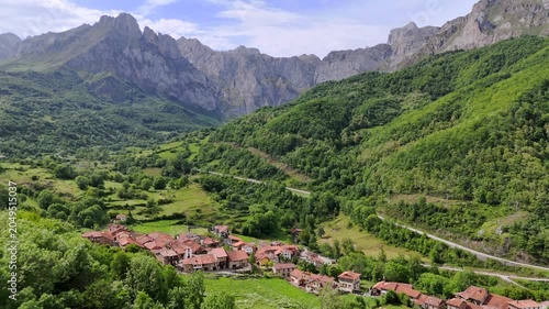 Drone shot moving forward above a rustic alpine village in Cantabria, Spain near Fuente De. Scenic aerial view of mountain landscape with the majestic Picos de Europa Central Massif in background.