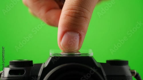 Close up of a finger pressing the top button of a camera on a green screen background.