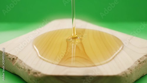 Golden oil pouring and spreading on natural stone coaster with green background.
