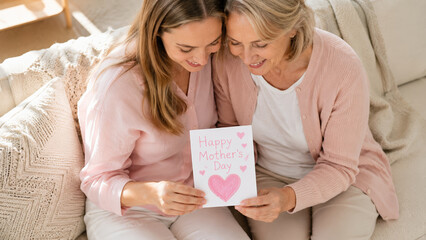 Mother daughter smiling together holding handmade Happy Mother Day card, cozy home setting