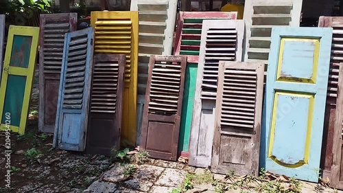 Panning shot of various colorful vintage javanese wooden shutters leaning against a wall for traditional home decoration or upcycling materials