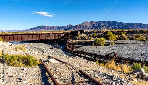 Twisted and mangled railway tracks lead to a collapsed bridge over a dry riverbed in a desolate landscape