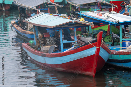 A colorful traditional wooden fishing boat powered by an engine docked in a harbor in Cilacap, Indonesia.