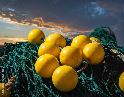 Close-up of yellow buoys nestled within a green fishing net, bathed in the warm light of a sunset