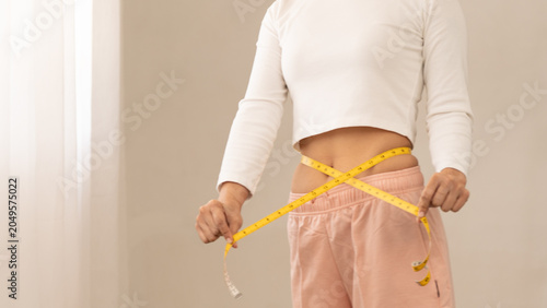 Fotografie woman measuring waist with yellow tape at home, weight loss and fitness concept, body shape control, healthy lifestyle, diet progress
