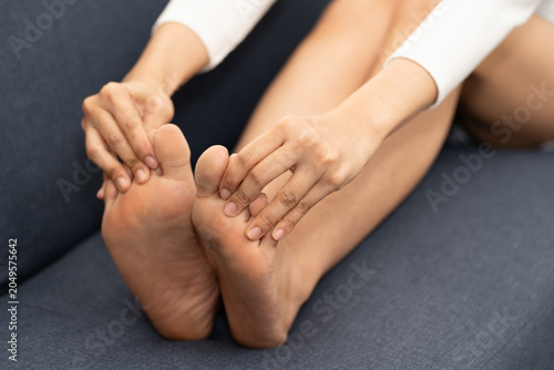 Foto Close up of Asian woman sitting on sofa holding feet, suffering from numbness and tingling in toes, foot pain, nerve problem and health issue at home
