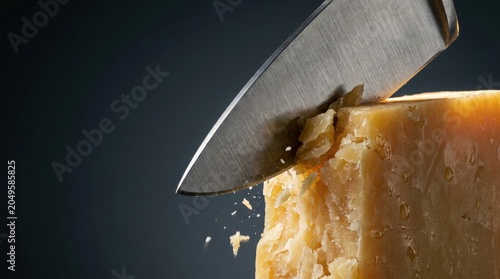 Close-up of knife cutting parmesan cheese with crumbs flying