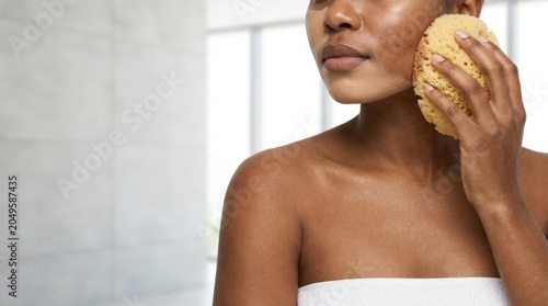 Woman cleansing textured skin with sponge in bathroom