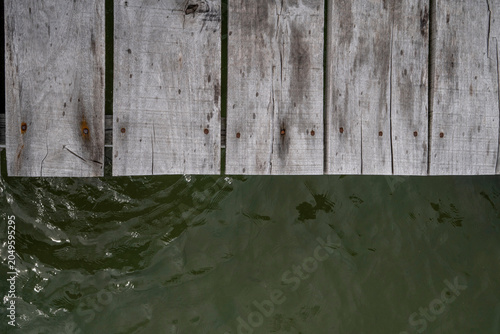 Fotografie Close-up of weathered wooden dock planks with rusty nails meeting murky green water surface below