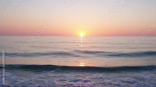 The sequence of frames depicts a serene ocean scene during sunset. The sun is positioned low on the horizon, casting a warm, golden glow across the calm water