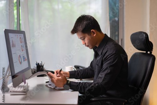 Business Professional Reviewing Financial Reports and Taking Notes at Office Desk During Data Analysis