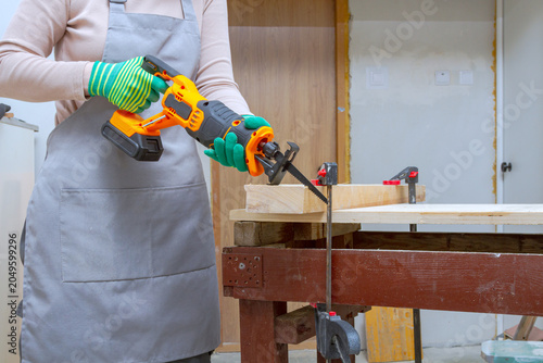 Foto Woman carpenter using reciprocating saw to cut wooden plank on workbench