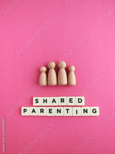Wooden family figures discussing shared parenting on pink background