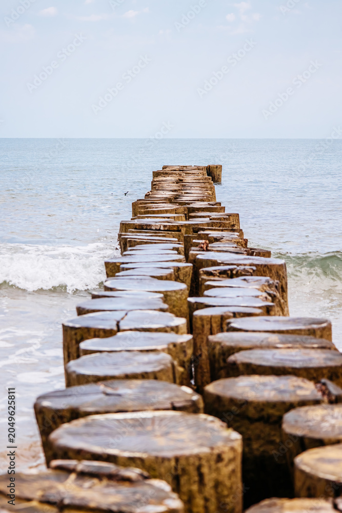 Fototapeta premium Weathered wooden groynes extending into the calm sea at sandy beach