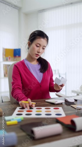 Asian designer woman selecting color palette material sample furniture design project creative studio workspace home office environment planning