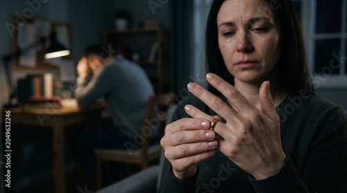 Crying woman taking off wedding ring in front of depressed man. Couple experiencing marital crisis and separation. Sadness and conflict in relationship, divorce, breakup concept.