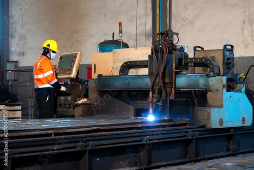 Industrial factory worker operating automated laser metal cutter machine, engineer technician control panel automated laser metal cutter machine heavy industry steel manufacturing factory production