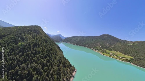 scenic aerial footage pilot point of view, of turquoise lake in a narrow valley of french alps under blue sky and reflection of the moutain on the calm waters