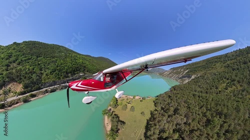 aerial footage, dynamic selfportrait of light airplane flying at low altitude over turquoise lake in a norrow valley of the french alps under blue sky 