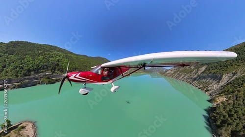 aerial footage, dynamic selfportrait of light airplane flying at low altitude over turquoise lake in a norrow valley of the french alps under blue sky 