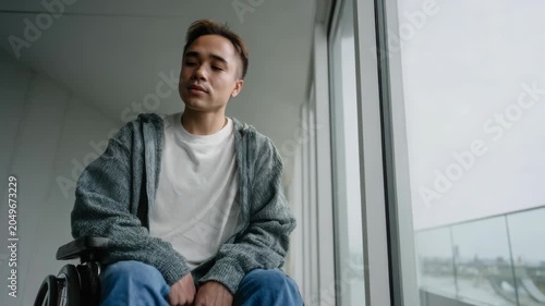 Young Man in Wheelchair Looking Out Window, Hopeful and Reflective Mood