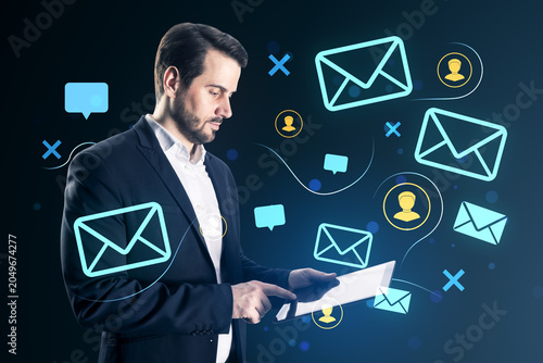 Business professional using tablet surrounded by glowing mail icons on dark b...