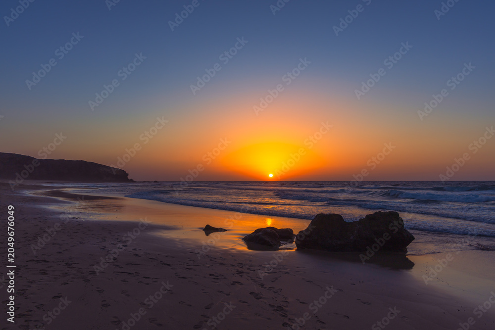 Obraz premium Vibrant Golden Sunset Over Atlantic Ocean Horizon From Sandy Beach With Rocks