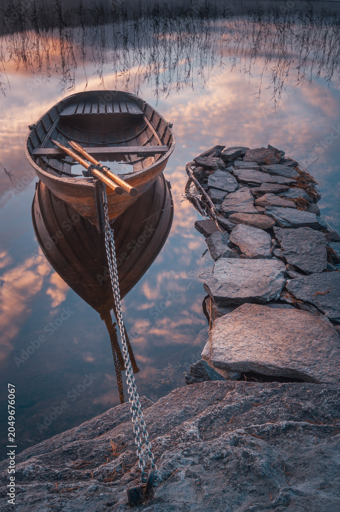 Obraz premium Row boat on still lake with stones and reflections at sunset in Sweden