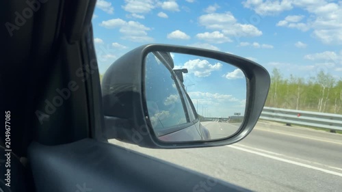 Car side mirror reflecting highway under blue sky with clouds, suitable for travel concept background