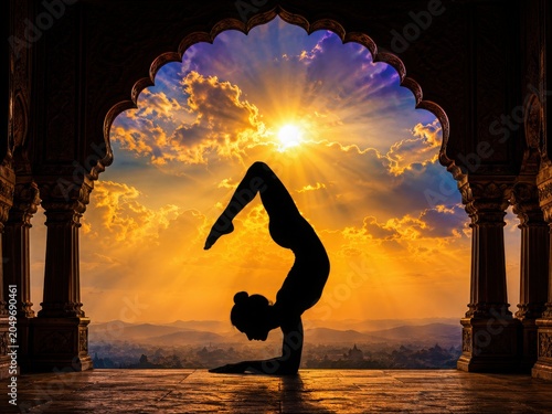 Yoga silhouette in scorpion pose at sunrise, spiritual meditation in ancient temple archway, wellness and mindfulness practice during golden hour