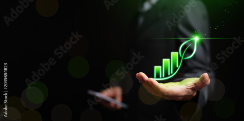 Business professional with glowing green growth chart shaped as a leaf above an open hand. ESG performance, sustainable growth, green investment, climate responsibility, and corporate sustainability.