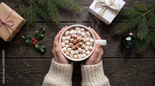 Hands holding hot chocolate with marshmallows among Christmas decorations
