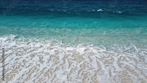 Aerial view of calm ocean waves breaking on a sandy beach, showcasing tropical summer travel and vacation