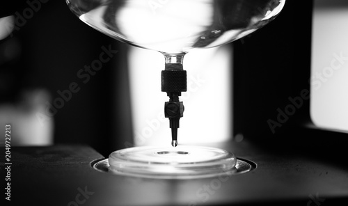 Фотография Monochrome close-up of a laboratory drip apparatus releasing a single liquid dro