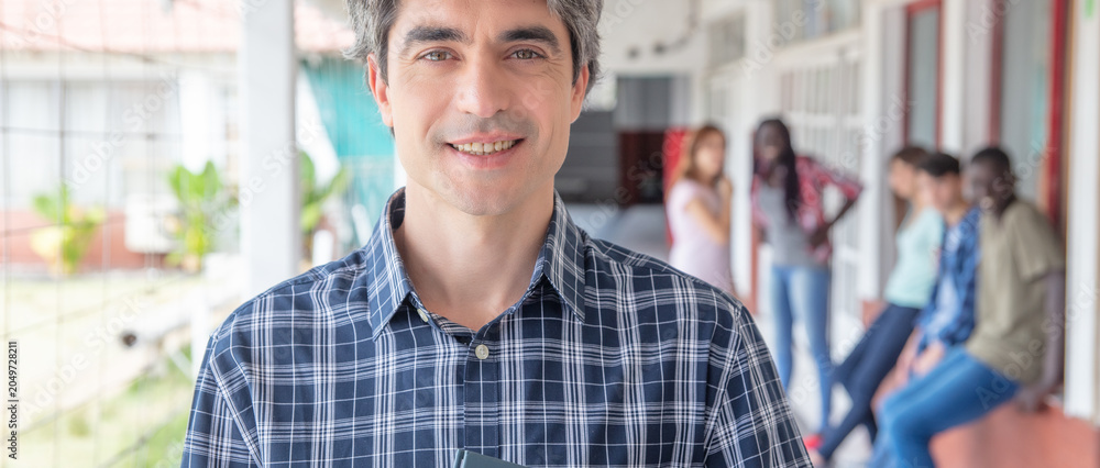 Obraz premium Happy teacher standing in the school hallway, group of students behind him