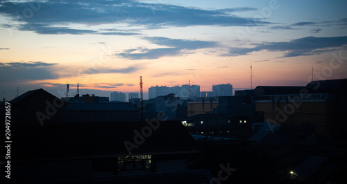 Urban city skyline at twilight with colorful sunset clouds and silhouetted buildings, capturing a peaceful evening atmosphere in a modern metropolitan landscape