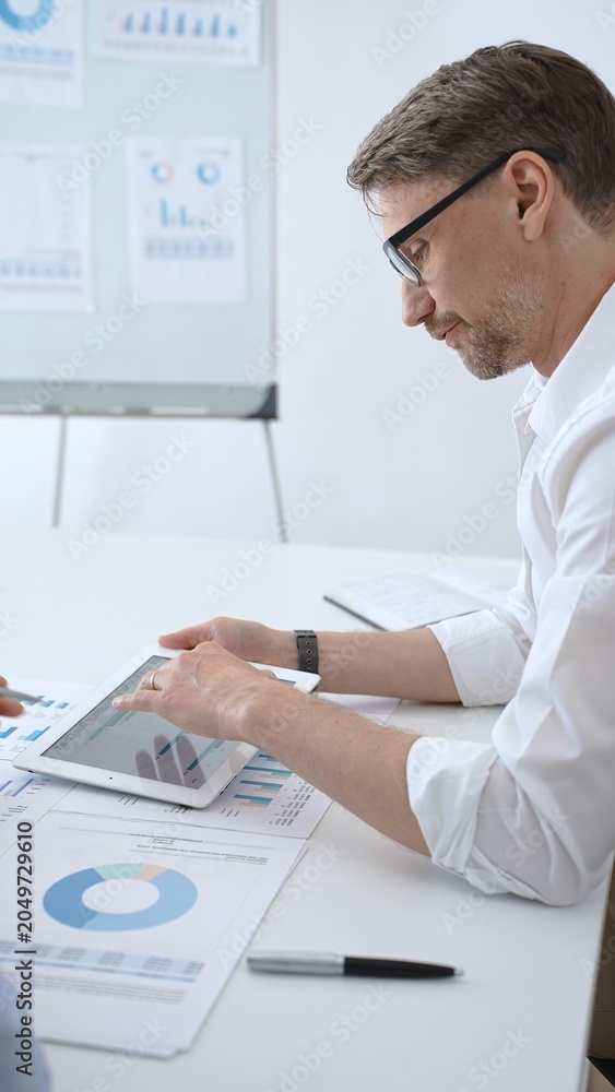 Obraz premium Business professional leading meeting, analyzing financial data and marketing reports on tablet during corporate presentation, discussing strategy with colleagues