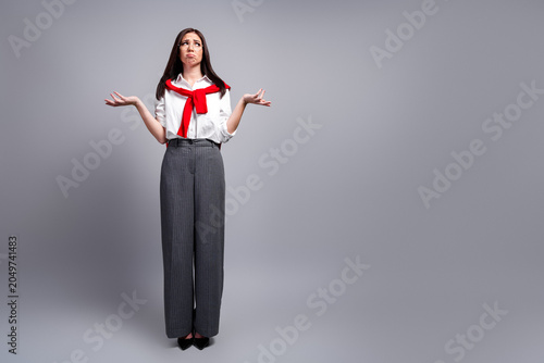 Confused businesswoman shrugging with upturned palms in studio portrait showing uncertainty, frustration and contemplation while wearing glasses, red sweater and pinstripe trousers