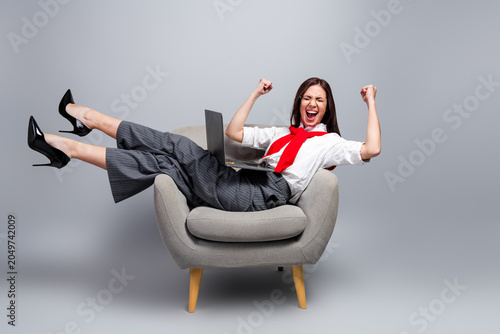 Foto Excited business woman celebrating success on laptop while reclining in armchair
