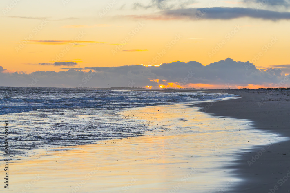Fototapeta premium Early morning sunlight peeks through clouds, casting golden reflections on the wet sand